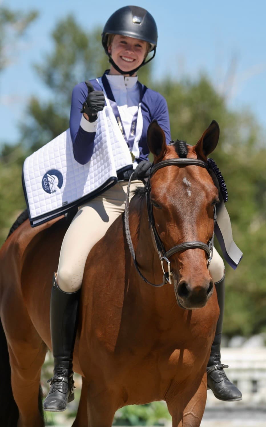 Tully giving a thumbs-up from horseback with a ribbon on her horse's bridle.